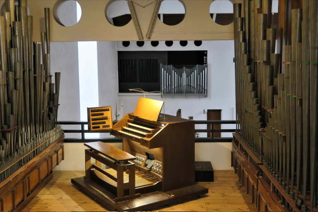 Orgelspieltisch, umgeben von vielen großen, freiliegenden Metallpfeifen.