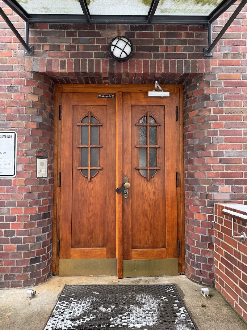 Doppelte Holztür mit kleinen Rundbogenfenstern in einer Ziegelsteinfassade.
