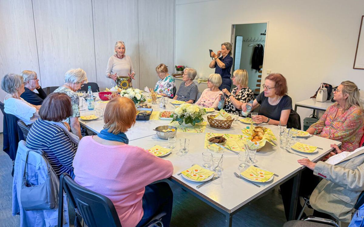 Gruppe von Frauen sitzt an einem Tisch, eine Frau steht und spricht.