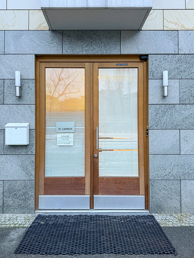 Moderne hölzerne Doppeltür mit Jalousien in einer grauen Steinmauer.
