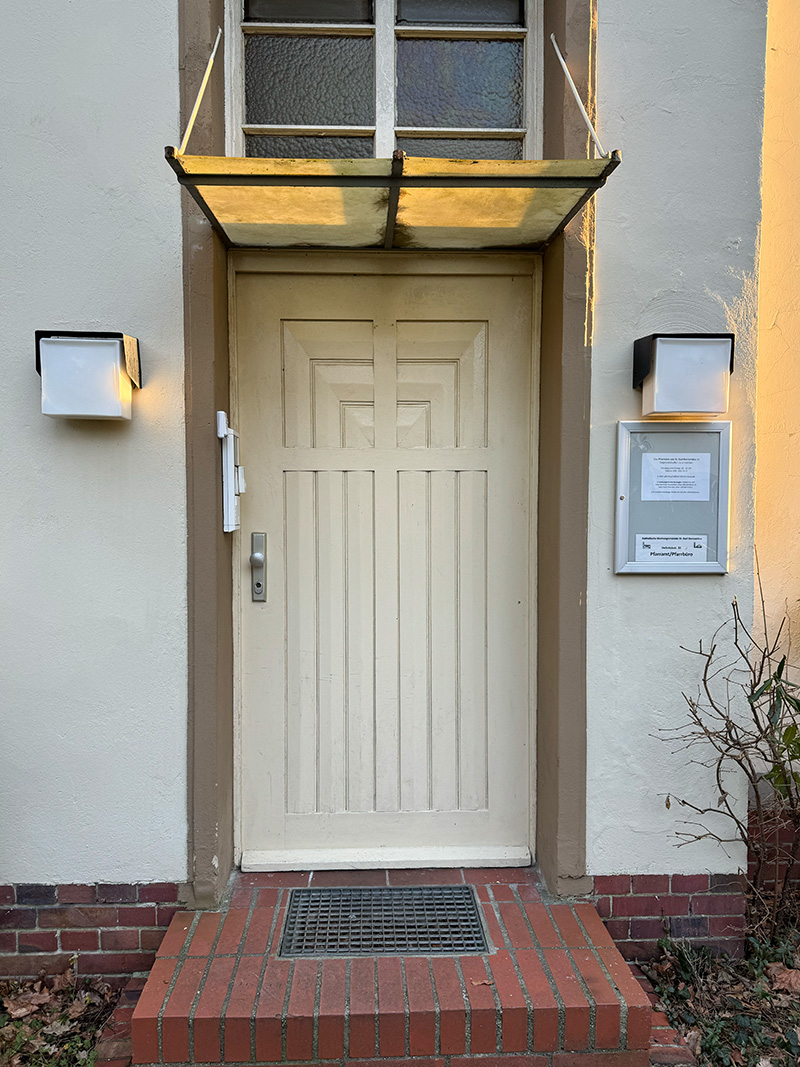 Einfache weiß gestrichene Tür unter einem kleinen Vordach an einem Stuckgebäude.